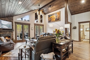 A spacious living room with a fireplace, leather furniture, and large windows offering a view of the outdoors.