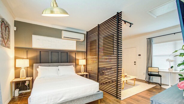 Ein modernes Schlafzimmer mit einem großen Bett, Nachttischlampen, einem Schreibtisch und einer Topfpflanze.