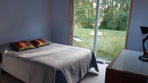 A bedroom with a bed, two pillows, a desk, and a view of a garden through a sliding door. - Cabin near Frutillar Lake Llanquihue (Casma)