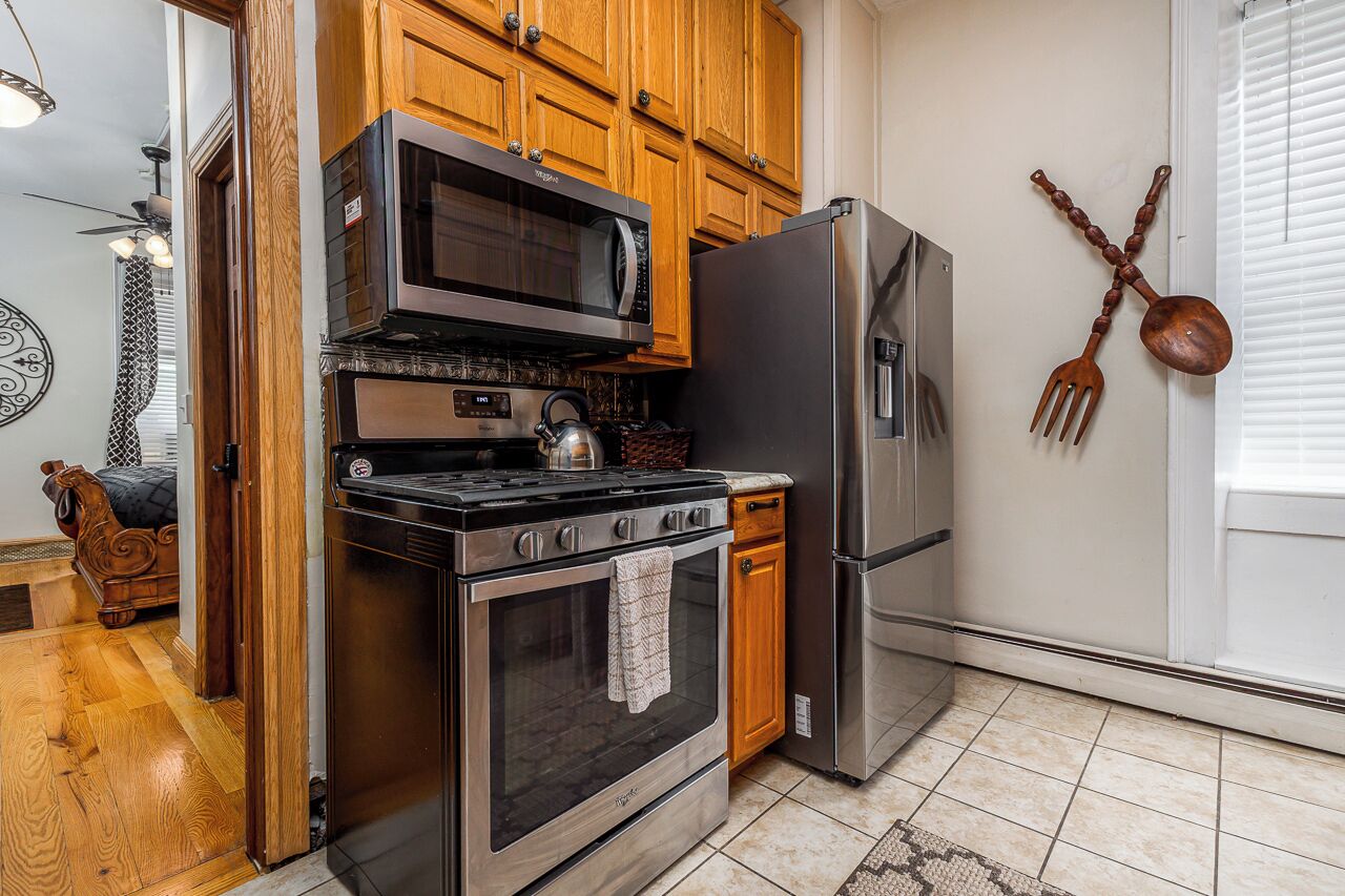 Una cocina con armarios de madera, un refrigerador de acero inoxidable, un microondas, un horno y una tetera.