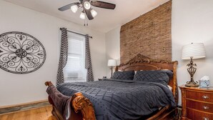 A bedroom with a wooden bed, a ceiling fan, a decorative wall piece, a nightstand with a lamp, and a window with blinds. - Check It Out! Great Location Large Priv w/Parking (Dubuque)
