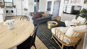 Una sala de estar moderna con sofá, mesa de comedor, sillas, televisor y zona de cocina con electrodomésticos.