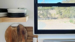 Una cocina con un ventanal grande, una tabla de cortar de madera y platos apilados en un estante.