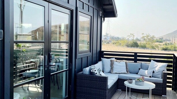 Una terraza moderna al aire libre con sofá y mesa, puertas correderas de vidrio y vistas al paisaje.