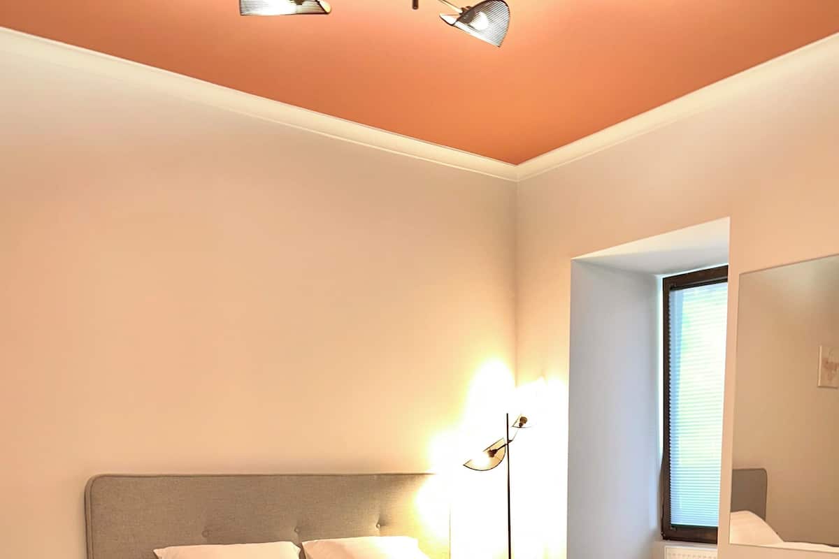 A neatly made bed in a hotel room with a grey headboard, a bedside table, and a floor lamp.