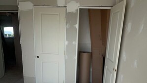 Habitación en renovación con techo y paredes expuestas, una puerta cerrada y un enchufe a la vista.