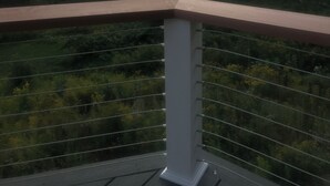 Un balcón con barandilla de metal que da a un paisaje boscoso y montañas distantes.