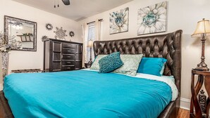 A bedroom with a tufted headboard, a large bed with teal bedding, a dresser, and decorative wall art. - Elegant 2 BR With Stunning Kitchen Prime Location! (Dubuque)