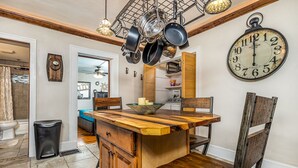 A kitchen with a wooden island, hanging pots, a large clock, and a view into the dining area. - Elegant 2 BR With Stunning Kitchen Prime Location! (Dubuque)