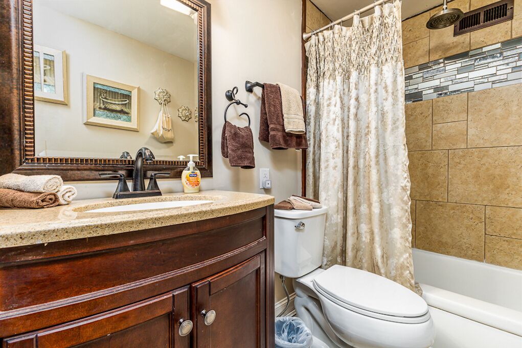 A bathroom with a wooden vanity, a large mirror, a toilet, and a shower area.