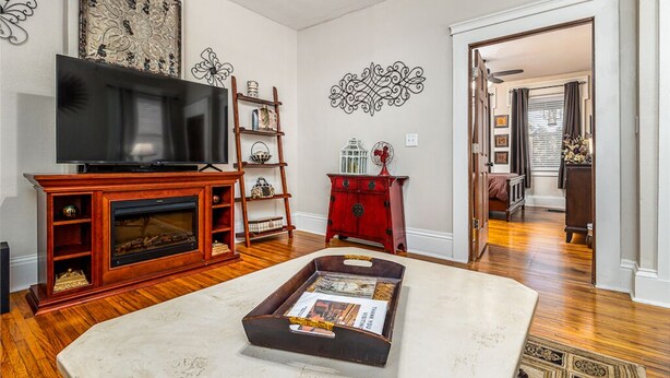 A living room with a TV, wooden entertainment unit, red dresser, decorative wall art, and a magazine tray. - Elegant 2 BR With Stunning Kitchen Prime Location! (Dubuque)