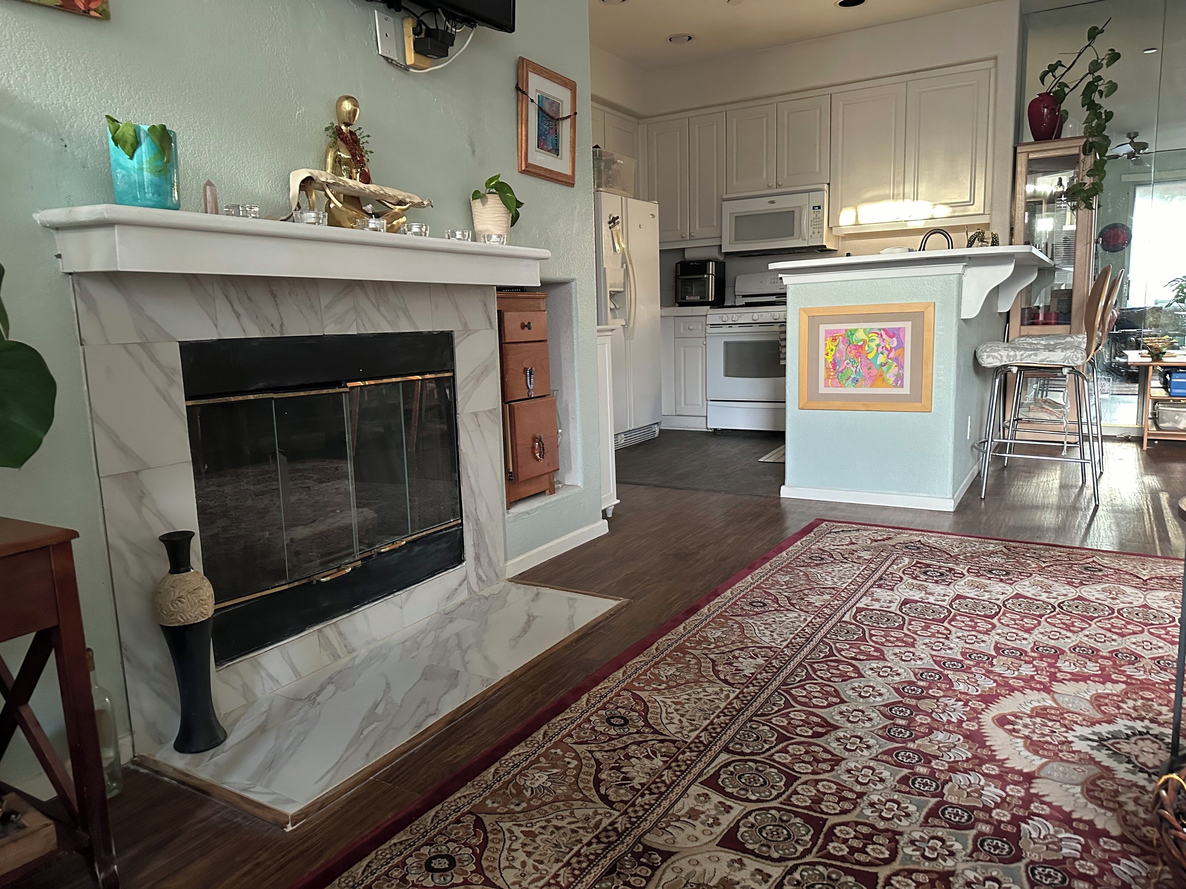A modern kitchen with white cabinets, a marble fireplace, and a patterned rug.