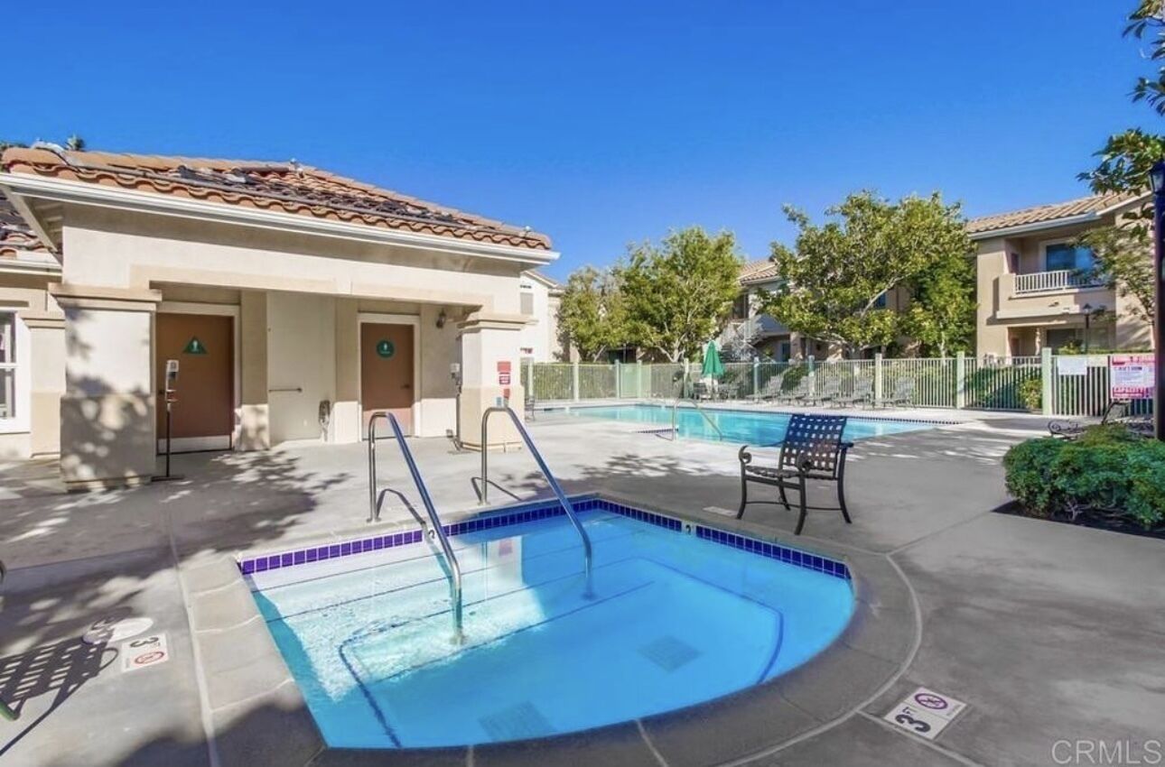 A swimming pool area with a pool, a chair, and a building with a tiled roof.