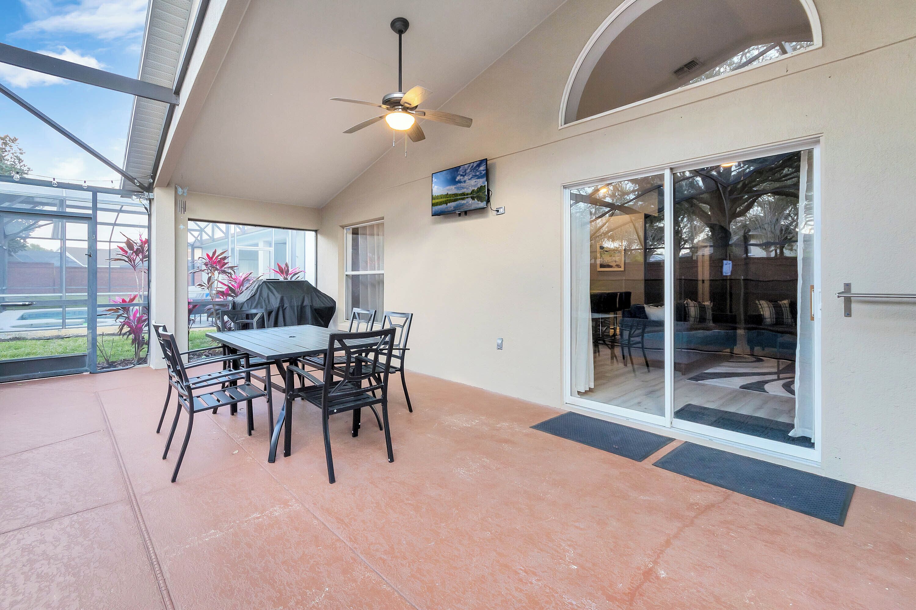 Une terrasse couverte avec une table et des chaises, un ventilateur de plafond et une porte-fenêtre coulissante donnant sur un espace intérieur.