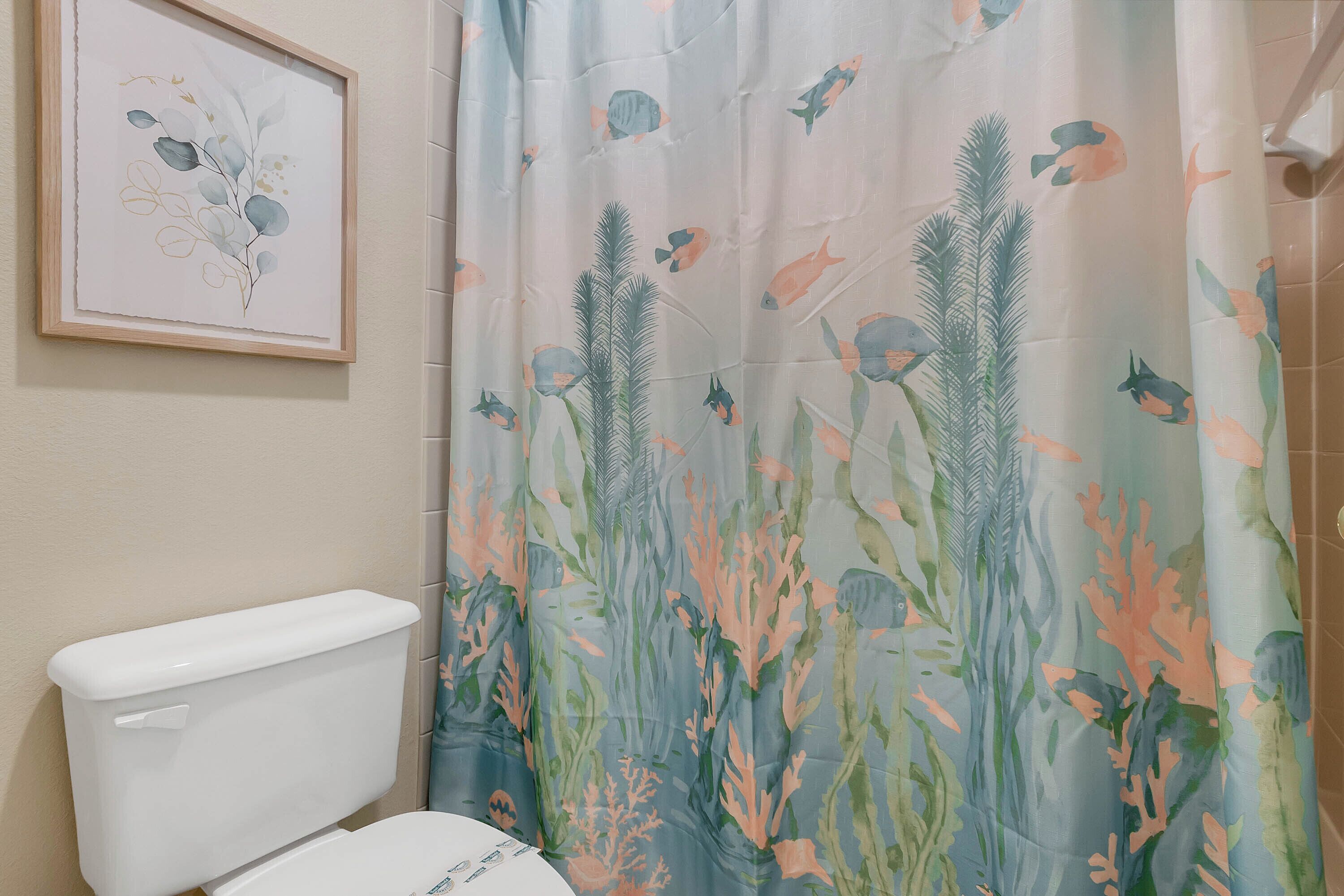 A bathroom with a toilet, a shower curtain with a marine life pattern, and a framed artwork on the wall.
