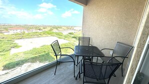 Ein Balkon mit Tisch und Stühlen, der auf eine grüne Landschaft und entfernte Gebäude blickt.