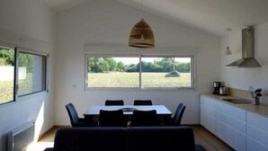 A modern kitchen with a dining area, large windows, and a view of a field.