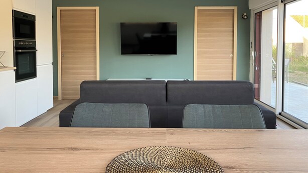 A modern living room with a flat-screen TV, a sofa, and a dining table.