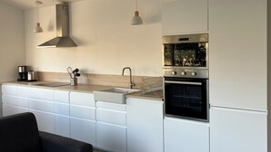 A modern kitchen with white cabinetry, a stainless steel range hood, a built-in oven, and pendant lighting.