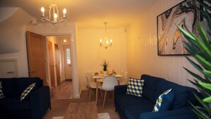 A living room with a dark blue sofa, a coffee table, and a chandelier. There is a dining area with a table and chairs. - Spacious 3 bed  town house in Bristol. (Bristol)