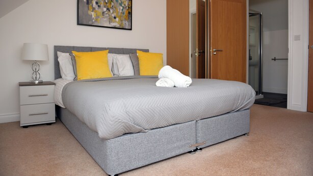 A bedroom with a bed, a nightstand, a lamp, and a door to a bathroom. - Spacious 3 bed  town house in Bristol. (Bristol)