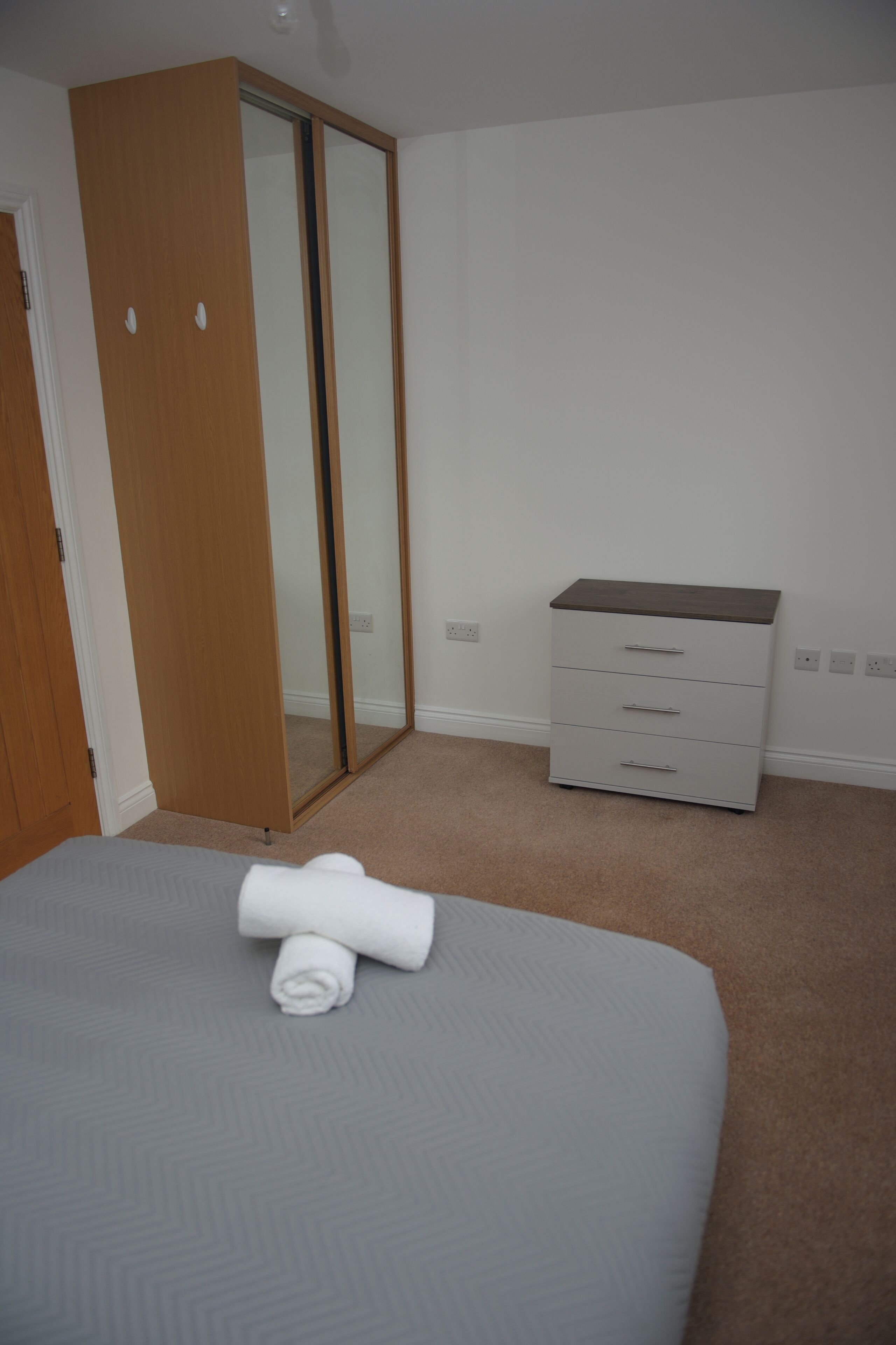 Un dormitorio con cama, armario de madera, cómoda y espejo.