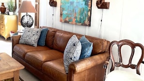 Ein Wohnzimmer mit einem braunen Ledersofa, einem Holzstuhl, einem Bild an der Wand und zwei Wandleuchten.