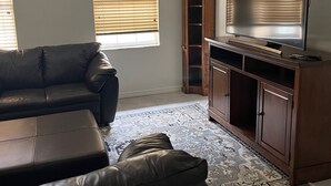 Un salon avec un canapé en cuir, un téléviseur posé sur un meuble en bois et un tapis à motifs.