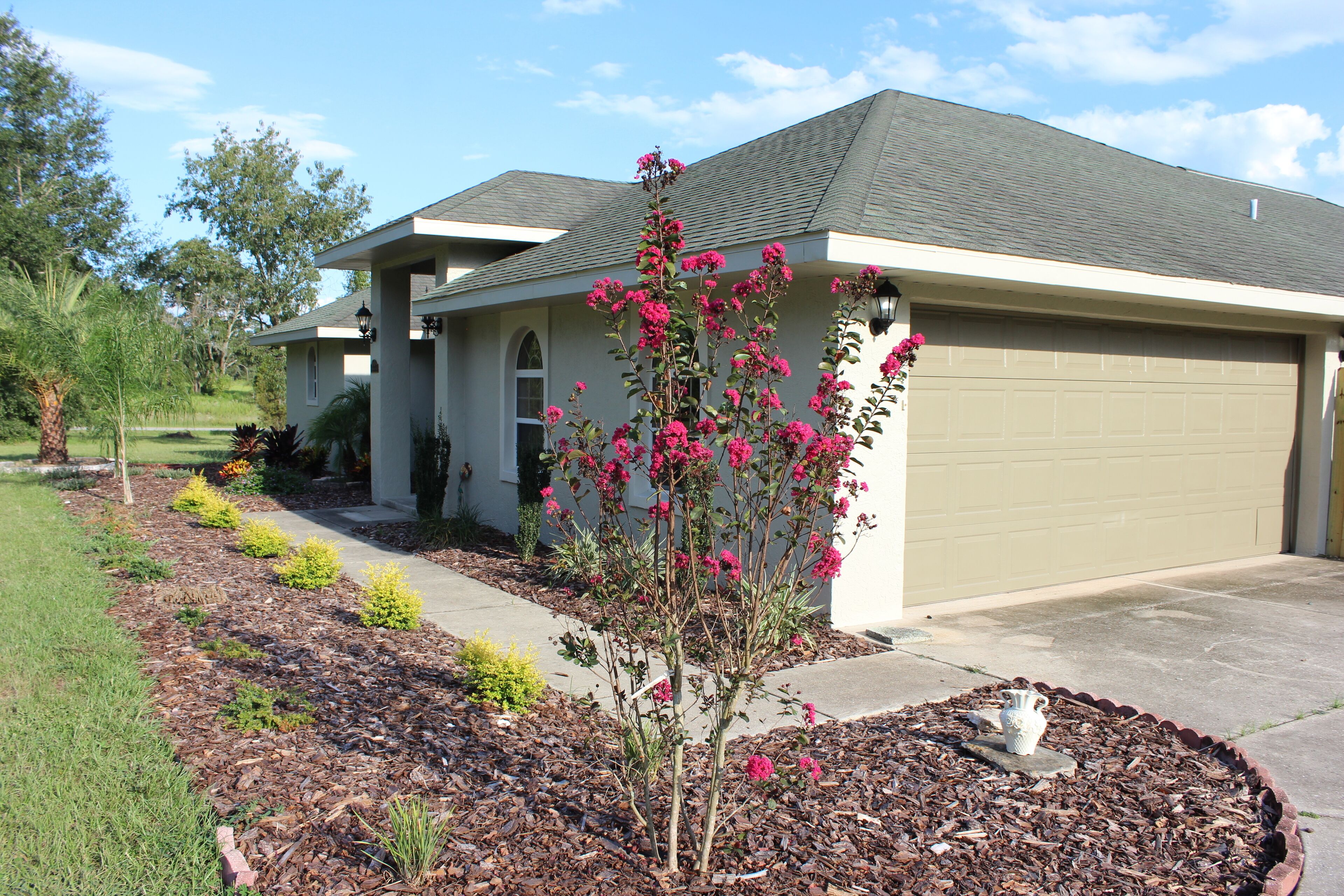 A residential house with a garage, a well-maintained garden with mulch and plants, and a clear sky.