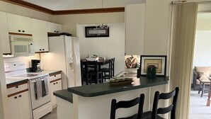 Une cuisine compacte dotée d’un îlot central, de meubles blancs et d’un coin repas avec des chaises.
