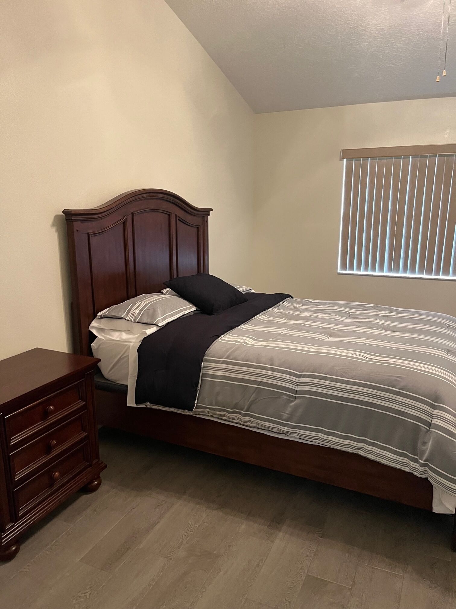 Un dormitorio con una cama de madera, una mesita de noche, una ventana con persianas y un aparador de madera.