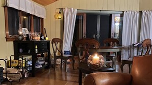 A cozy living room with wooden floors, a brown leather sofa, a dining table with chairs, and a kitchen area with a cabinet and various items.