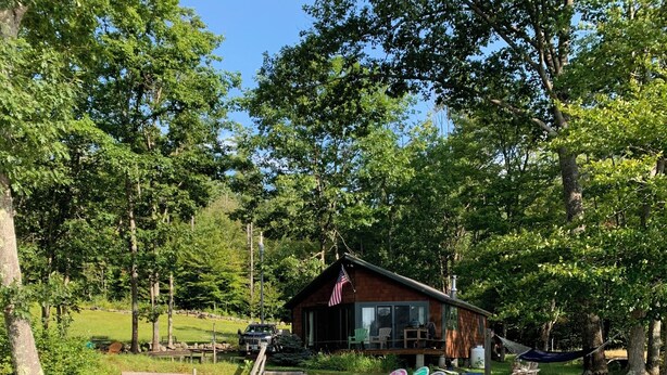 A cabin with a dock extending into a calm body of water, surrounded by lush greenery and trees.