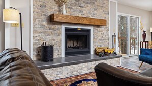 A living room with a stone fireplace, leather sofas, a patterned rug, and a large window. - The Getaway at Wintergreen Resort (Wintergreen Resort)