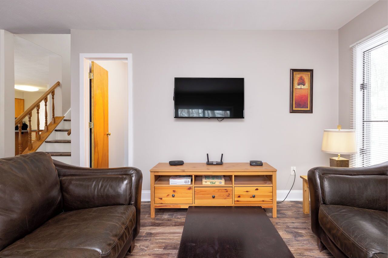 Una sala de estar con televisor, muebles de madera, sofá y una escalera.