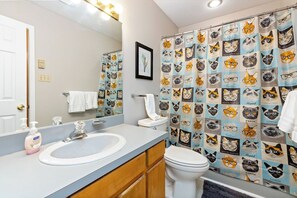 Une salle de bain avec un lavabo, un miroir et des toilettes. Le rideau de douche est orné d’un motif représentant des chats.