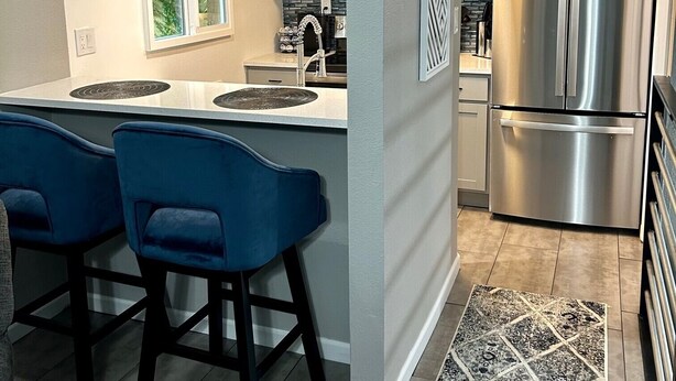 Una cocina moderna con una isla central, taburetes de bar, electrodomésticos de acero inoxidable y una alfombra estampada.