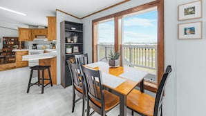 Een moderne keuken met houten kasten, een eethoek met een houten tafel en stoelen, en een groot raam met uitzicht op de omgeving.
