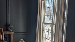 A room with a dark wall, a large window with curtains, a wooden table, a chair, and a small plant. - Southern charm meets Lake Norman/Charlotte - pet friendly (Cornelius)
