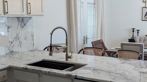 A modern kitchen with a marble countertop, a sink, and light-colored cabinets. There are two pendant lights above the sink and a chair in the background. - Southern charm meets Lake Norman/Charlotte - pet friendly (Cornelius)