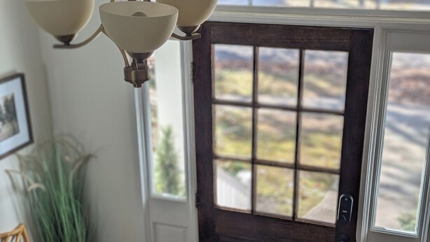 A dark wooden door with a grid pattern, a wicker chair with a cushion, a hanging light fixture, and a view of a landscape through the window. - Southern charm meets Lake Norman/Charlotte - pet friendly (Cornelius)