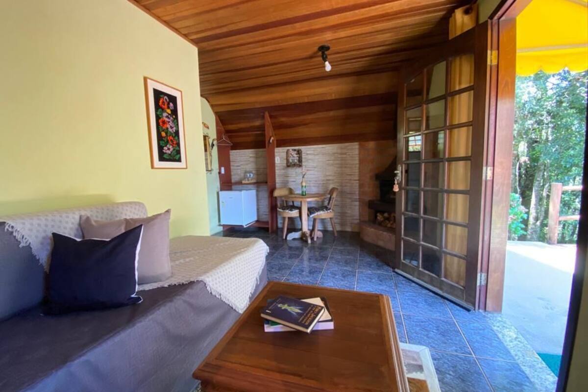 A cozy living room with a wooden ceiling, a sofa with cushions, a coffee table with books, a fireplace, and a large sliding glass door leading to an outdoor area.