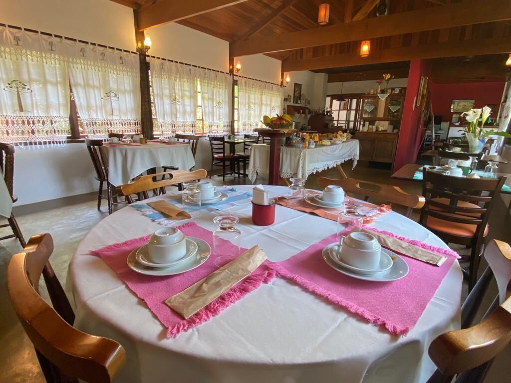 A dining area with round tables set for tea service, featuring white tablecloths, pink placemats, and white teacups.