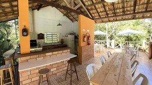 An outdoor patio with a brick bar, wooden table, and white plastic chairs. - Pousada Sotaque Mineiro (Cunha)