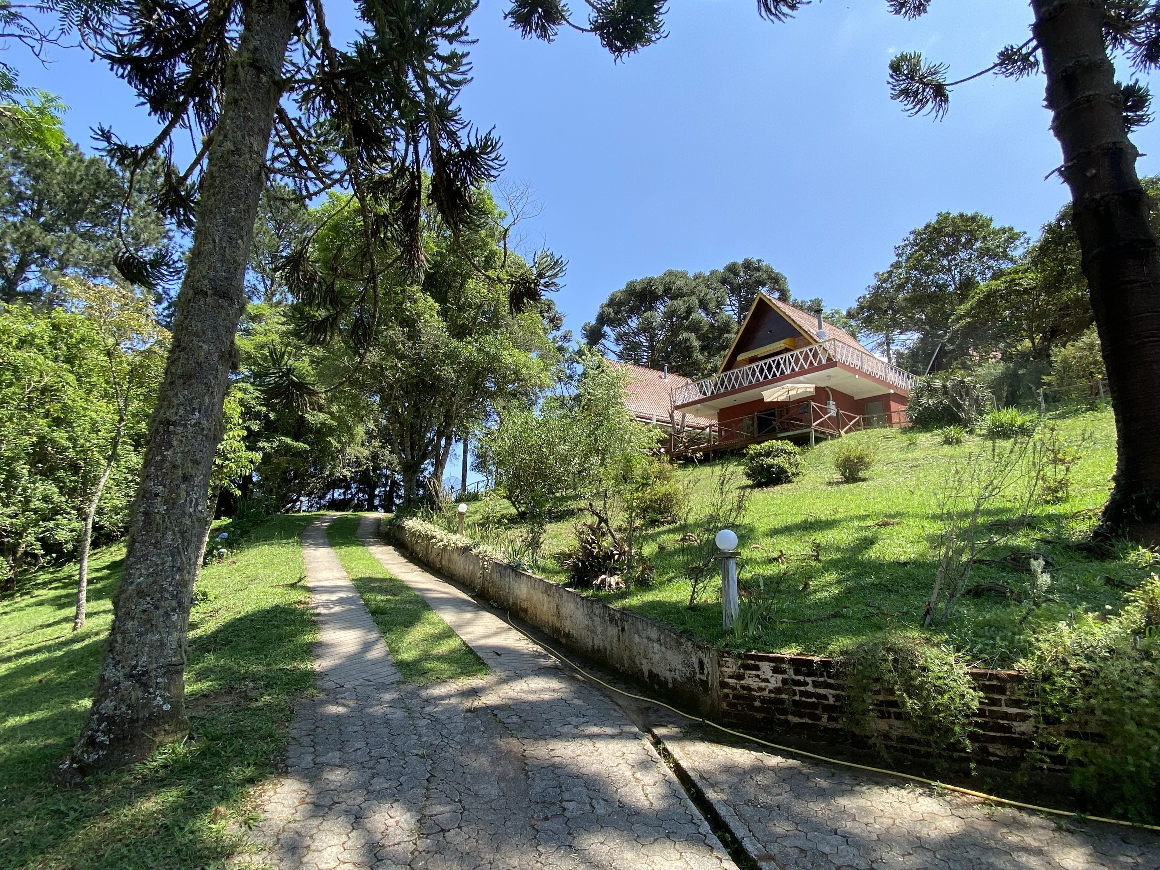 Uma casa com telhado vermelho e uma varanda, cercada por árvores e um gramado.