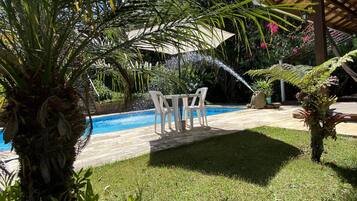 Zona de piscina con una palmera, área de descanso cubierta y césped.
