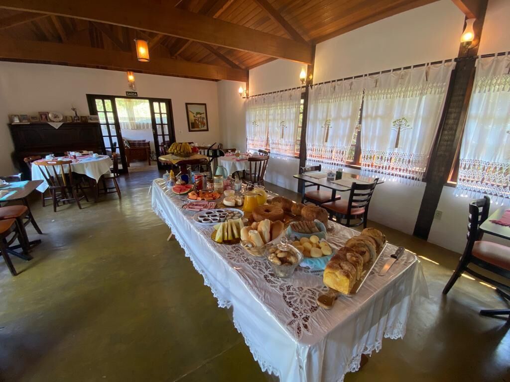 Un espace repas avec une longue table recouverte de diverses pâtisseries et de pains, entourée de chaises et de petites tables.