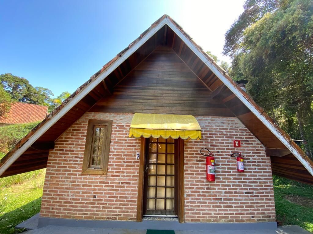 A small brick building with a triangular roof, a yellow awning, a single door with a window, and two fire extinguishers mounted on the wall.
