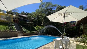 A swimming pool with a tiled deck, surrounded by a garden with a staircase and a pergola with an umbrella. - Pousada Sotaque Mineiro (Cunha)