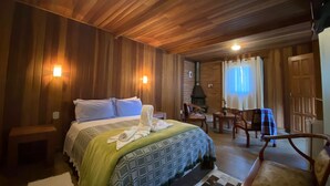 A cozy room with a wooden ceiling, a bed with a green and patterned blanket, a fireplace, and a seating area with chairs. - Pousada Sotaque Mineiro (Cunha)